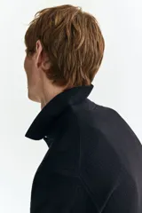 Remera polo de manga corta en punto texturizado negro, con cuello y tapeta de tres botones. Remate acanalado en puños y bajo, con un corte estándar.