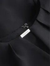 Blusa negra de poliéster reciclado con mangas cortas, cuello redondo, cierre con cremallera en la espalda y abertura en la parte delantera con barra metálica.