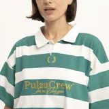 Remera tipo polo de manga corta, color verde oscuro, con cuello y abertura frontal. Presenta un estampado dorado en el pecho con el texto "PulauCrew" y un pequeño logo de corona de laurel bordado.
