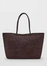Bolso tipo shopper color marrón, confeccionado en paja trenzada con dos asas largas para llevar al hombro.