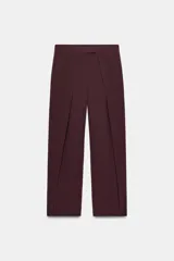 Pantalón de tiro alto con diseño barrel, presenta pliegues frontales marcados y bolsillos laterales. Cuenta con cierre frontal mediante cremallera, botón interior y gancho metálico oculto.