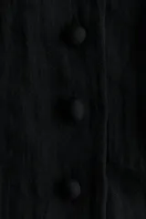 Vestido corto negro con escote redondo, mangas cortas abullonadas y cierre frontal de botones forrados. Cuenta con costuras moldeadoras en la cintura y falda con bajo globo fruncido.
