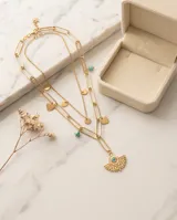 Collar doble de acero con baño de oro, compuesto por una cadena de eslabones alargados y una cadena fina con dijes colgantes de corazones, círculos y un dije central en forma de ojo turco con diseño de abanico.