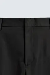 Pantalón de vestir gris oscuro, corte ancho (flare fit) y tiro alto, con bolsillos laterales y falsos bolsillos de vivo en la parte trasera. Presenta un cierre frontal con cremallera y gancho oculto, y botones a presión ocultos en el bajo.