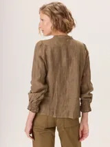 Camisa de lino rústico color marrón oscuro, con cuello mao, botones frontales y detalles de volados en el frente. Mangas largas con puños fruncidos.