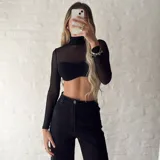 Top negro de mangas largas y cuello alto, confeccionado en tejido de red transparente. Incluye un corpiño bandeau negro con frunce en el centro.