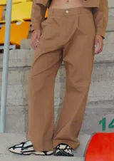 Pantalón camel de gabardina elastizada, corte sastrero, tiro bajo, con bolsillos delanteros, botón metálico y tajo en el lateral interno.