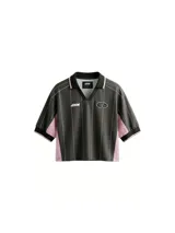 Camiseta tipo crop top de manga corta con cuello polo, confeccionada en tela técnica dry fit. Presenta un diseño a rayas verticales blancas sobre fondo marrón, con paneles laterales en color rosa y detalles en negro en el cuello y los puños.