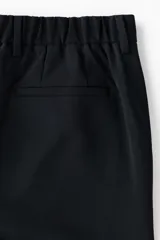 Pantalón sastrero de corte slim fit y color negro, con cierre frontal de botón, bolsillos laterales al bies y bolsillos posteriores ojalados. Cuenta con trabillas para cinturón y pretina elástica en la parte posterior.