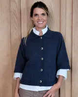 Cardigan de lana lambswool color azul oscuro, con cuello clásico, cierre frontal de botones y mangas cortas con terminación acanalada. Presenta dos bolsillos frontales y diseño de punto tejido.