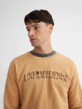 Buzo color tostado con cuello redondo, corte central y mangas raglán. Presenta un estampado frontal con la palabra "UNFRMDENIM" en negro.