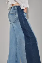 Jean de corte wide leg con diseño bicolor, presentando un panel central en denim lavado claro y paneles laterales en denim azul oscuro. Posee tiro alto y cierre frontal con botón.