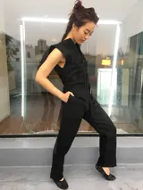 Mono largo de lino color beige, con detalle plisado en el frente, escote en V, sin mangas, lazo en la cintura, cierre invisible delantero y bolsillos laterales.