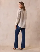 Blusa blanca de lino y rayón, con cuello a la base, escote en V y abertura con botones. Tiene bolsillos en la parte delantera y mangas largas regulables con presilla y botón.