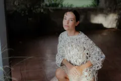 Buzo de tejido de punto calado con diseño de red, cuello redondo y mangas largas abullonadas. Presenta una textura jaspeada en tonos gris y blanco.