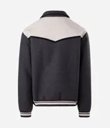 Campera de estilo varsity confeccionada en polyvelour, con diseño bicolor en gris oscuro y crema. Presenta cuello tipo polo, cierre frontal con botones a presión, mangas largas y puños y cintura con terminación en ribana a rayas.