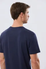 Remera azul marino de manga corta con cuello redondo, confeccionada en mezcla de algodón y poliéster. Presenta un estampado frontal circular de inspiración vintage con diseño de velero y tipografía alusiva a clubes deportivos.