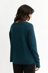 Sweater azul petróleo de tejido de punto, con cuello redondo y botones decorativos en los laterales.