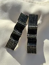 Par de aros colgantes con forma geométrica irregular, recubiertos de strass negros sobre base plateada.
