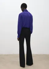 Blusa de poliéster color azul, con cuello alto, lazada integrada, cierre lateral con botones y mangas largas abullonadas con puños ajustados.