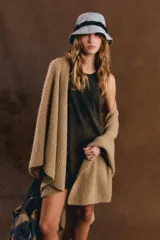 Poncho de punto grueso y sin mangas, color marrón tostado, abierto como capa y con ruedo asimétrico.