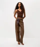 Pantalón de jean color marrón con corte baggy holgado, tiro medio y cierre frontal con cremallera y botón. Incluye un pañuelo estampado decorativo en la cintura.