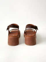 Sandalias de plataforma color chocolate con tira frontal ancha de gamuza y tira al tobillo con hebilla metálica ajustable.