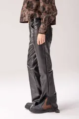 Pantalón de cuero vacuno negro, de tiro alto y corte recto con aberturas en los tobillos. Presenta detalles de costuras y bolsillos traseros.