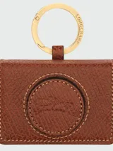Llavero de cuero vacuno color marrón con diseño de estuche tipo cámara, argolla metálica dorada grabada con el logo de la marca y detalle de logo en relieve en el centro.