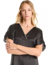 Vestido midi negro de satén con escote en V profundo y ribete de strass. Presenta una silueta relajada y fluida con corte oversized, mangas cortas amplias y una pequeña tabla central debajo del escote que genera un drapeado natural.