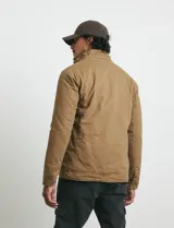 Campera de tejido técnico elástico en color verde oliva, con capucha integrada, cierre frontal y bolsillos con cierre en el pecho. Cuenta con forro interior de micro polar y diseño funcional.