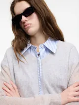 Sweater de punto fino color gris claro, con cuello en V y mangas largas. El tejido parece ser ligeramente transparente o muy liviano.