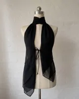 Top negro de estilo halter con cuello alto y abertura frontal profunda, ajustado mediante lazos. Confeccionado en tela semitransparente y ligera.