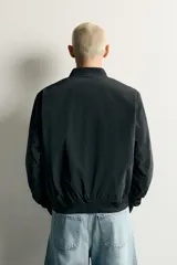 Cazadora bomber de tejido técnico ligero color marrón oscuro, con corte regular fit, cuello, puños y ruedo de rib elástico, bolsillos frontales de vivo y cierre frontal con cremallera.