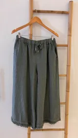 Pantalón capri color verde oliva de lino con cintura elástica ajustable con cordón, bolsillos laterales y terminación con flecos.