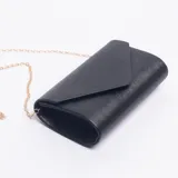 Sobre de mano tipo clutch color negro con textura lineal, solapa triangular y cadena metálica dorada extraíble.