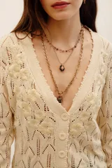 Cardigan de punto color beige con escote en V, cierre frontal con botones y detalles de flores bordadas en relieve a lo largo de la abertura. Cuenta con mangas largas y terminaciones en rib.