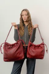 Bolso tipo shopper de cuero negro con diseño acolchado en patrón de rombos. Cuenta con cierre superior fruncido y correa de cadena metálica entrelazada con cuero.