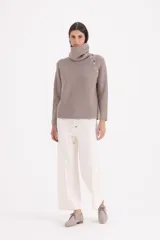 Sweater de punto color beige con cuello alto tipo polera, manga larga y detalle de botones decorativos en el hombro y cuello.