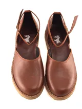 Zapato plano tipo bailarina o mary jane, color gris claro, con puntera redonda y tira de ajuste con hebilla en el tobillo. Suela negra.