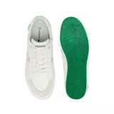 Championes Lacoste modelo L004, de diseño urbano en color blanco con detalles en gris claro. Presentan una silueta de perfil bajo con paneles de lona y refuerzos de gamuza en la puntera y el talón. Incluyen el icónico logo del cocodrilo metálico en el lateral del talón y una suela de goma vulcanizada.
