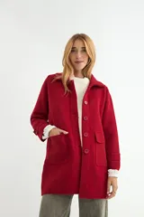 Abrigo de paño color rojo, con cuello camisero, cierre frontal de botones al tono y dos bolsillos frontales con solapa. Presenta mangas largas con detalle de trabilla en los puños.