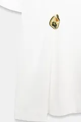 Camiseta de algodón compacto color negro, con cuello redondo, manga corta y detalle de aplique metálico en el frente que genera un ligero fruncido lateral.