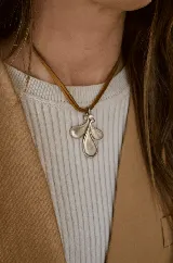 Collar con dije de metal plateado en forma de hojas estilizadas con un pequeño cristal incrustado, suspendido de una cinta de gamuza color marrón.