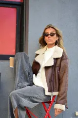 Campera de cuero sintético marrón con interior y detalles de corderito sintético blanco, cuello con solapas, cierre frontal y bolsillos con cremallera.