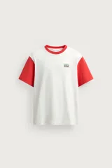 Remera de corte regular fit en color blanco con cuello redondo y mangas cortas en color rojo contrastante, y aplicación de parche bordado en el pecho.