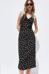 Vestido midi de lunares, color negro con lunares blancos, escote en V y mangas sisa con hombreras. Presenta frunces laterales en la cintura y cierre en la espalda con cremallera oculta.