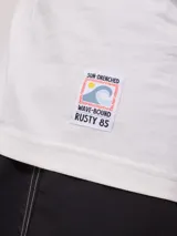 Remera blanca de algodón con cuello redondo y manga corta. Presenta un pequeño estampado frontal con el logo de Rusty y un diseño de tabla de surf.