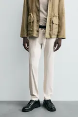 Pantalón chino de corte ajustado, color beige, con bolsillos laterales y bolsillos traseros de vivo. Cuenta con cierre frontal de cremallera y botón.