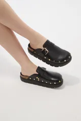 Suecos negros de estilo zueco con capellada de cuero sintético, detalle de hebilla metálica dorada y tachas decorativas alrededor de la suela. Poseen plantilla ergonómica y suela de plataforma dentada.